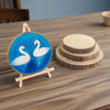 Decorative plate with swan design on a stand next to wooden coasters on a table.