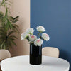 Black vase with flowers on a white table against a blue wall