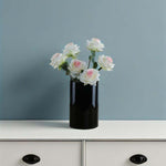 Black vase with white and pink flowers on a white surface against a blue wall