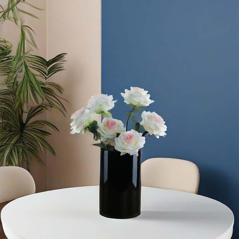Black vase with flowers on a white table against a blue wall