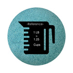 Sea Blue colored sand arranged in a circular shape on a white background colored sand in a circular shape with a measuring cup showing quantity.
