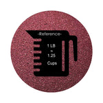 Burgundy colored sand arranged in a circular shape on a white background colored sand in a circular shape with a measuring cup showing quantity.