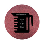 Burgundy Red colored sand arranged in a circular shape on a white background colored sand in a circular shape with a measuring cup showing quantity.