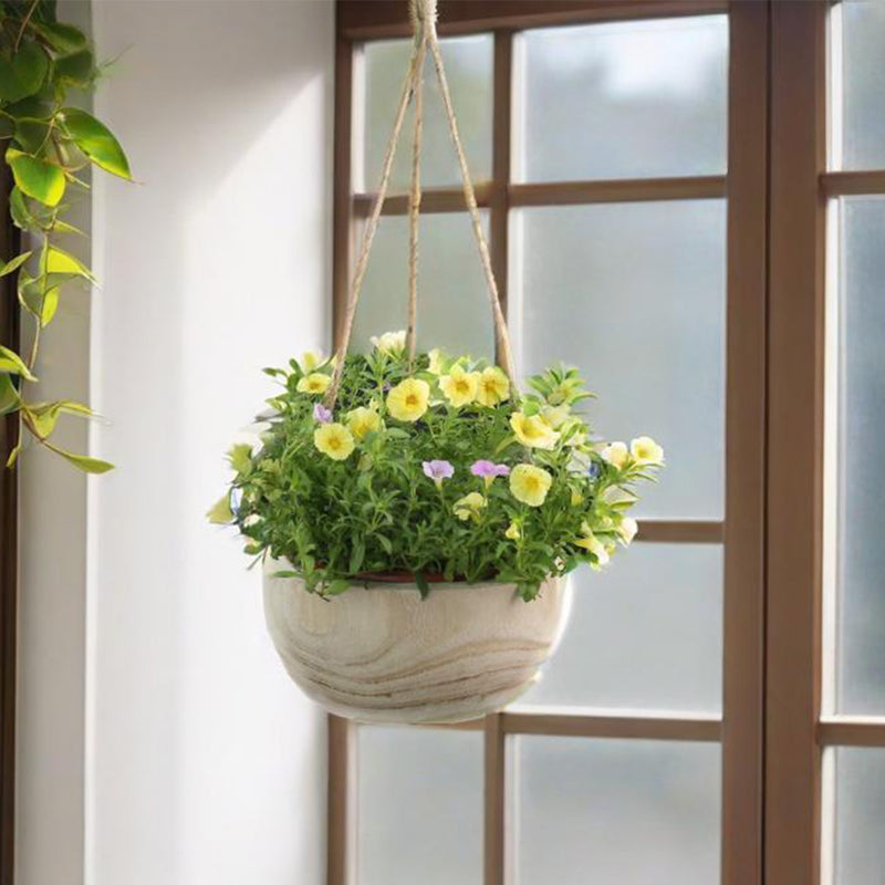 Hanging flower pot with greenery and yellow flowers in front of a window