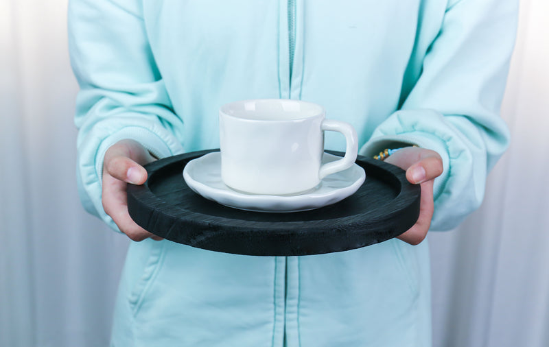 Person holding a white mug on a black tray with a light blue jacket.