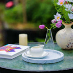 Table setting with a teacup, saucer, and decorative items on a marble tray outdoors.