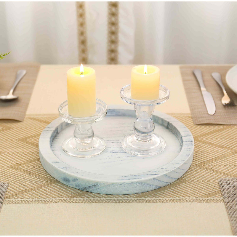 Two lit candles in glass holders on a decorative tray on a table setting.