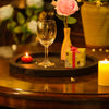 Wine glass, gift box, pink rose in a vase, and candles on a wooden table.