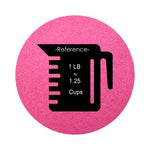 Fuchsia colored sand arranged in a circular shape on a white background colored sand in a circular shape with a measuring cup showing quantity.
